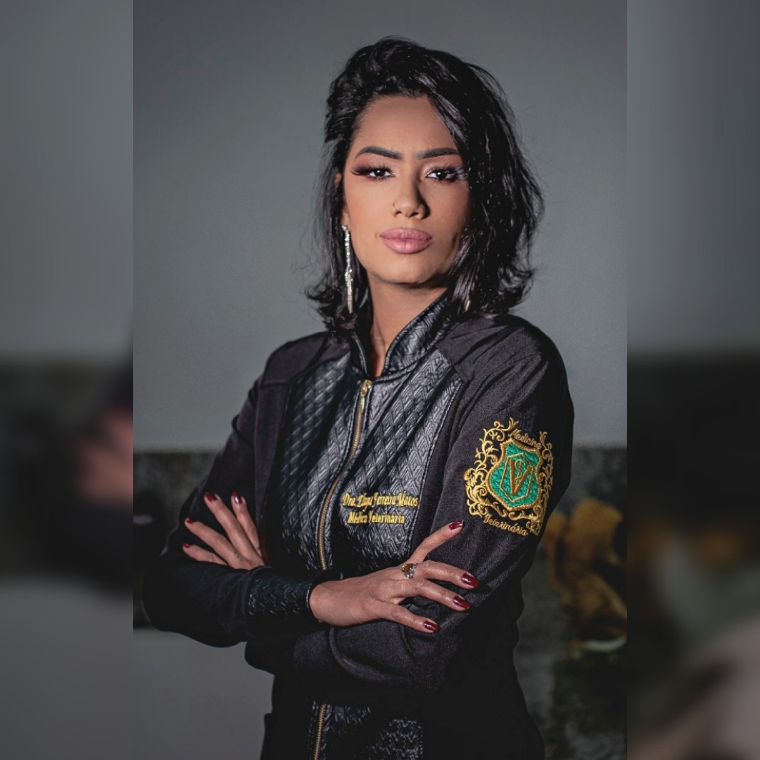Dra. Elayne Ferreira de braços cruzados, com jaleco preto bordado